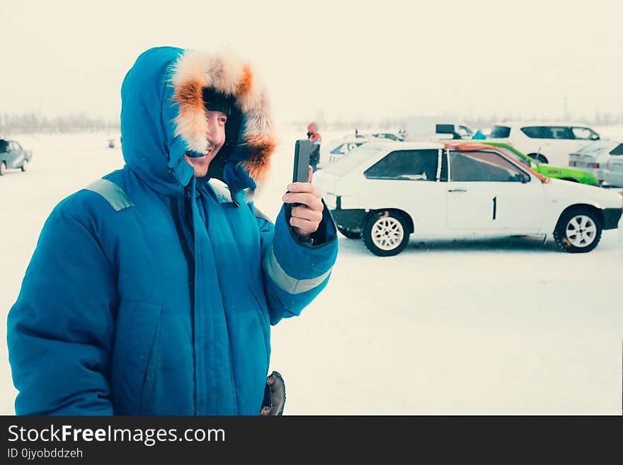 A young man in a blue down jacket talking on a smartphone in a thirty-degree frost. A young man in a blue down jacket talking on a smartphone in a thirty-degree frost