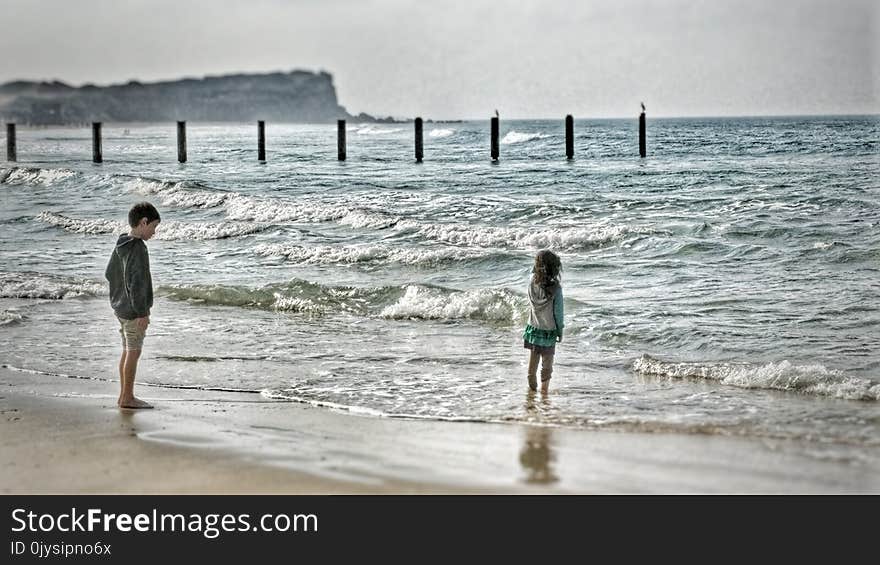 Two Young Children Standing On The Beach Watching The Waves