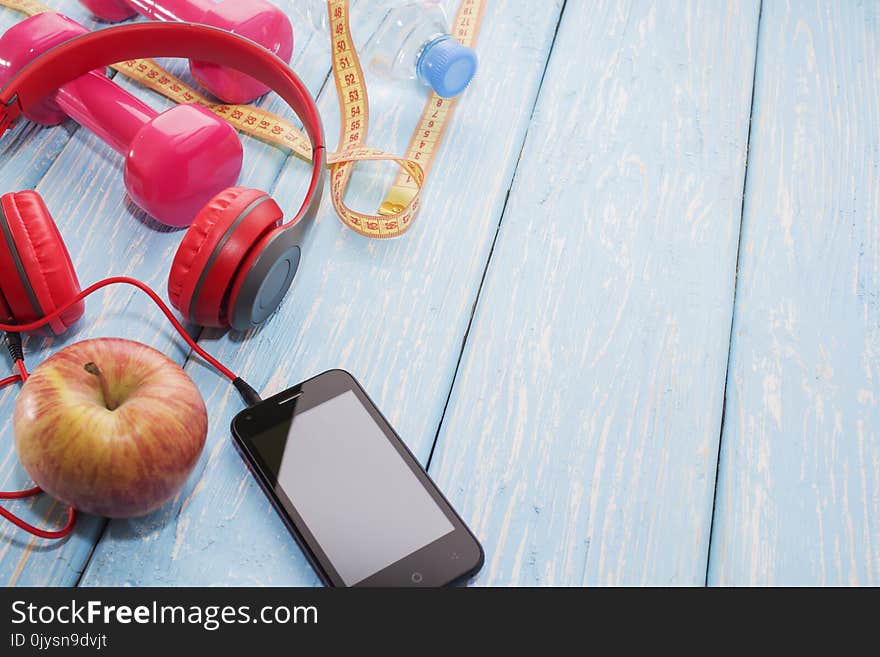 Fresh fruit with dumbbells on a wooden countertop, copy space, diet, and healthy food concept. Headphones and phone. Music in spor