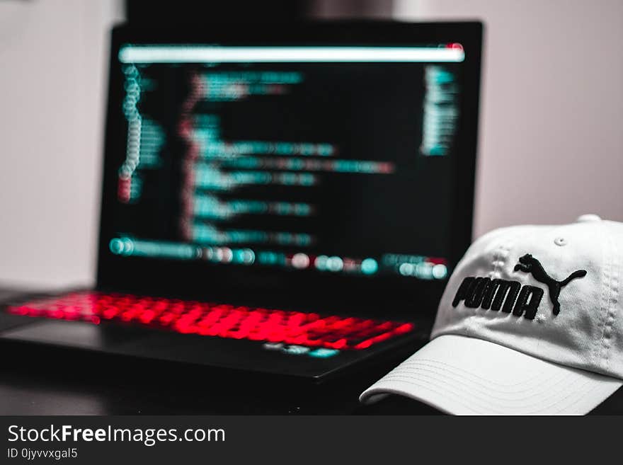 Black and Red Laptop Computer Beside White Puma Curve Brim Cap