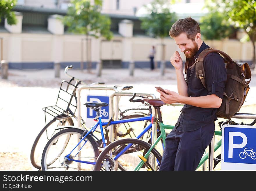 A handsome bearded male in casual clothing using a phone near bicycle parking. A handsome bearded male in casual clothing using a phone near bicycle parking.