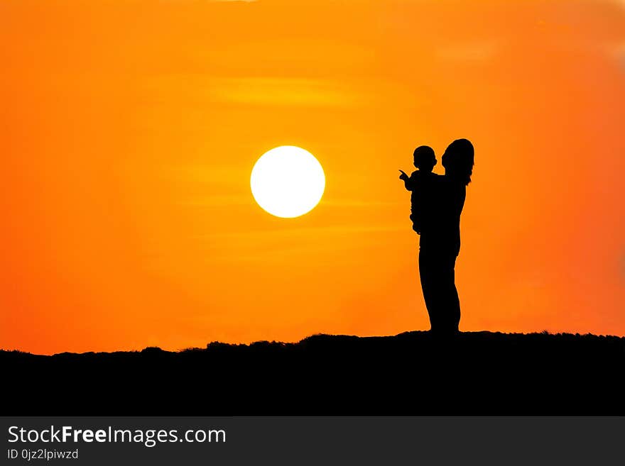 Black silhouette of a mother carrying her son watching the sunset on mountain orange background,Asia people