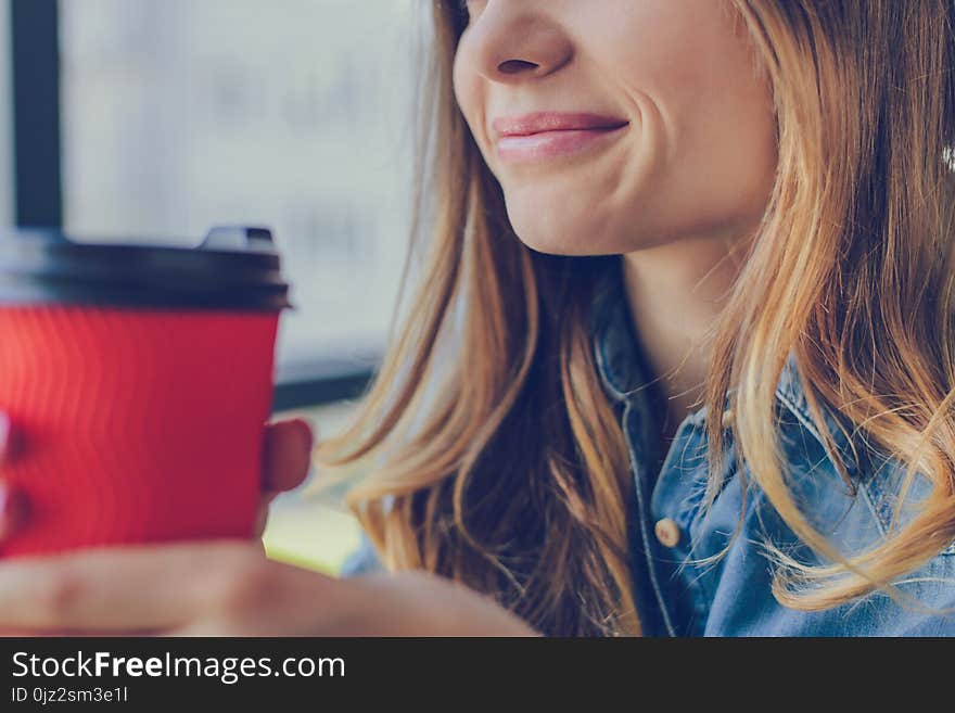 Concept of calmness and relaxation. Smiling woman holding a cup is going to drink coffee. She is sitting in a cafe near the window. Close up, cropped photo