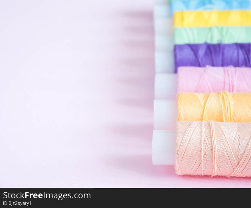 Colorful sewing buttons and thread on a pink background.