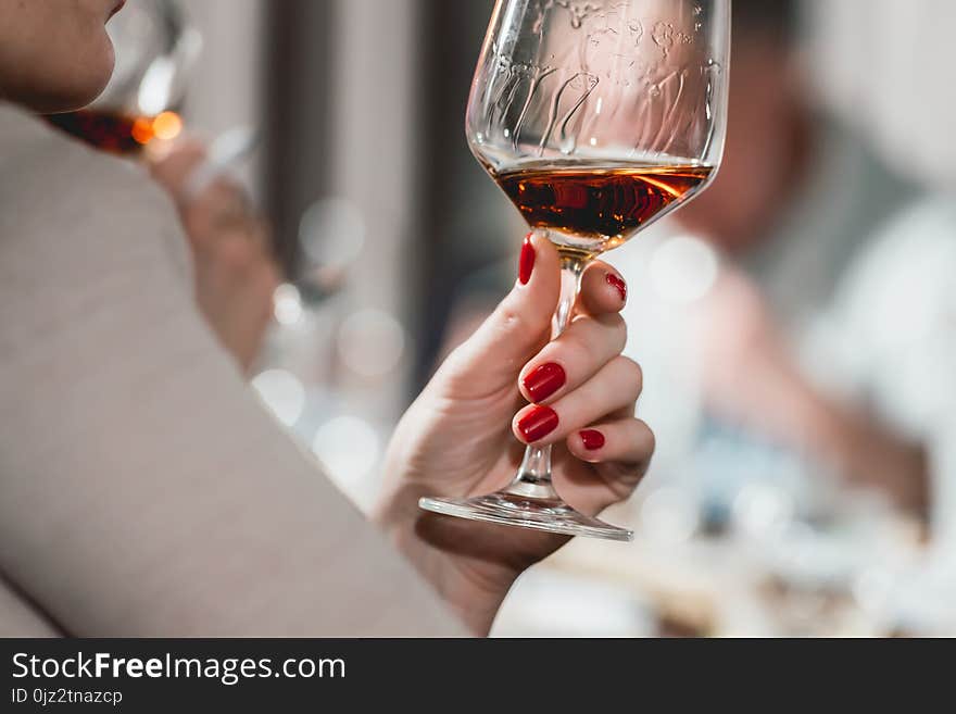 Woman Holds Glass Of Red Wine. People Consider The Color Of The Wine And Try How It Smells In Different Glasses