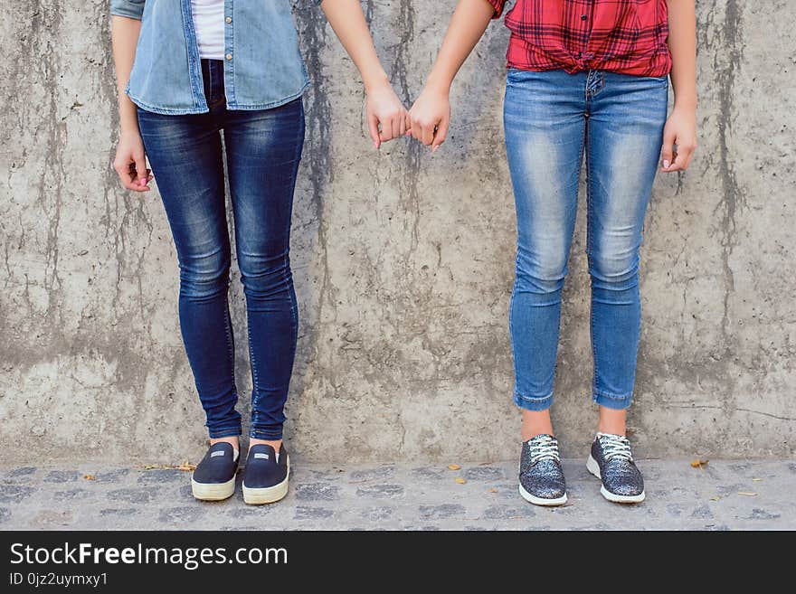 Help lesbians people comfort console concept. Close up photo of two cute lovely sweet teen age girls holding little fingers wearing stylish jeans isolated on concrete gray wall background