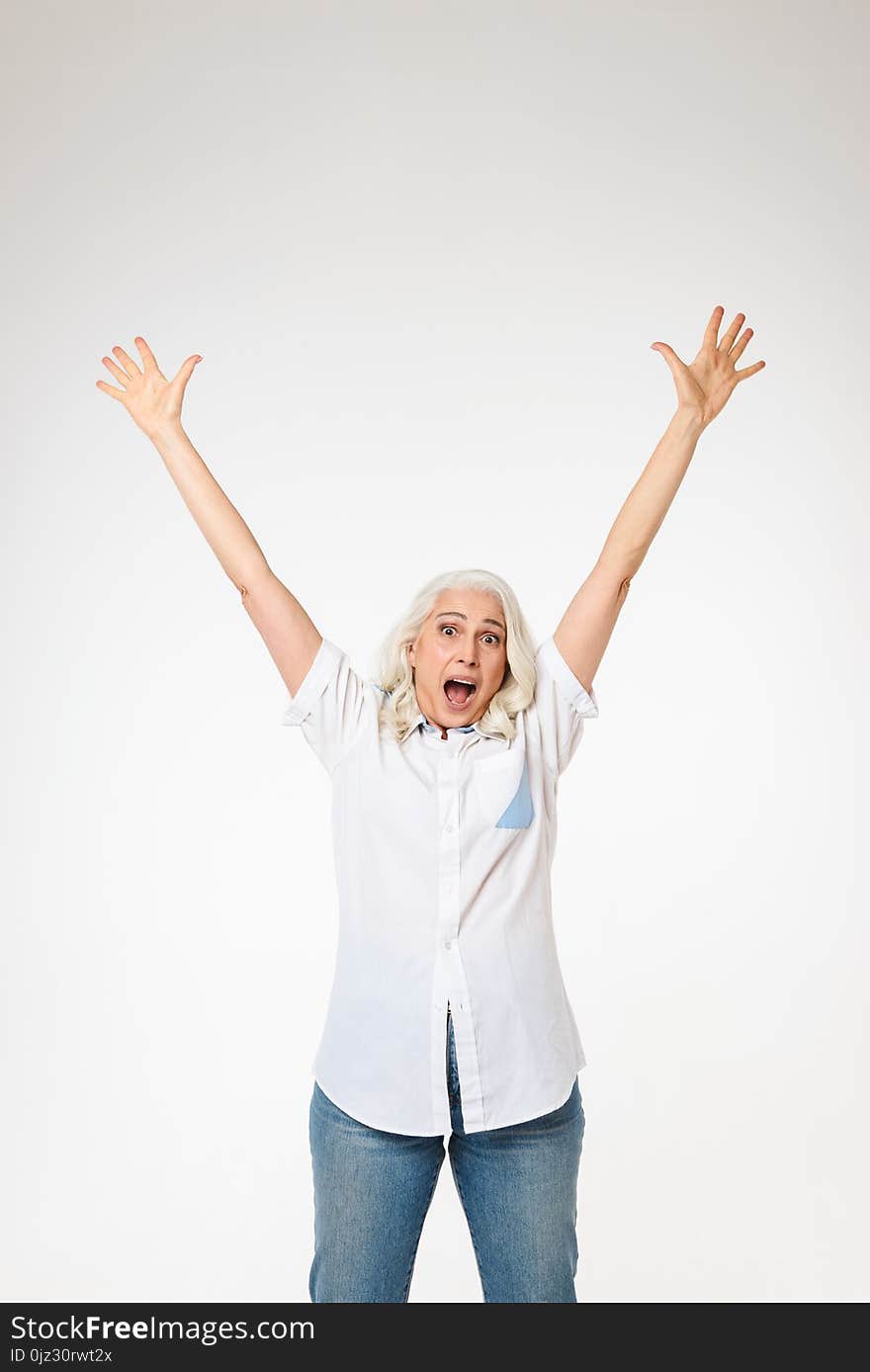 Beautiful female pensioner 60s with gray hair raising her arms and screaming like happy woman isolated over white background