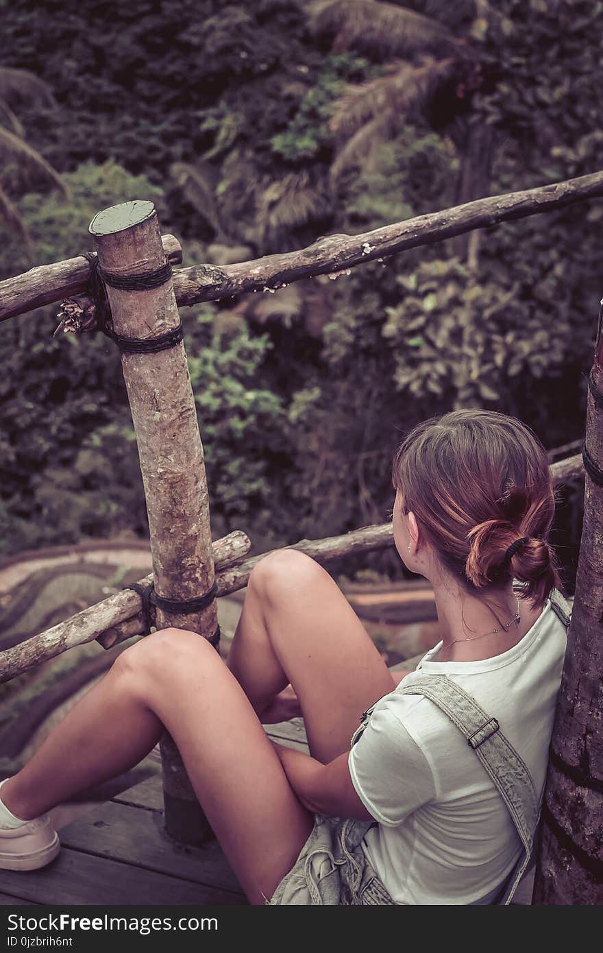 Woman Wearing White Shirt and Shortalls Sitting on Wooden Terrace