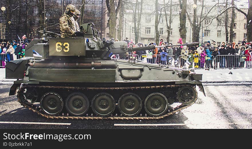 Two Soldiers Ride on Green Military Tank Surrounded With People