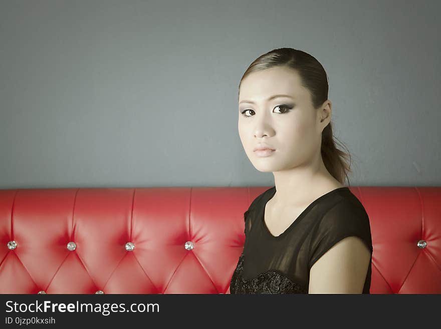 Beautiful Face Woman In Black Dress Sitting On Red Sofa