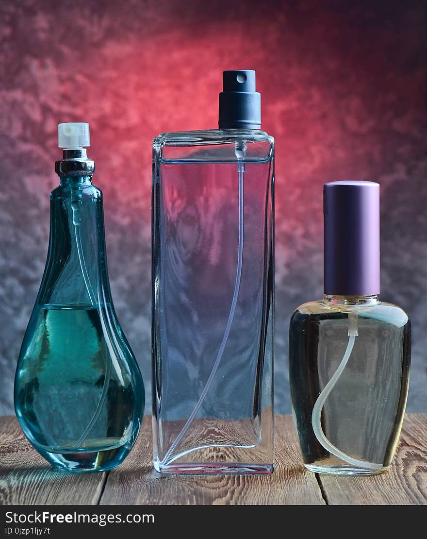 Three different bottles of perfume on a wooden shelf against the background of a concrete wall.