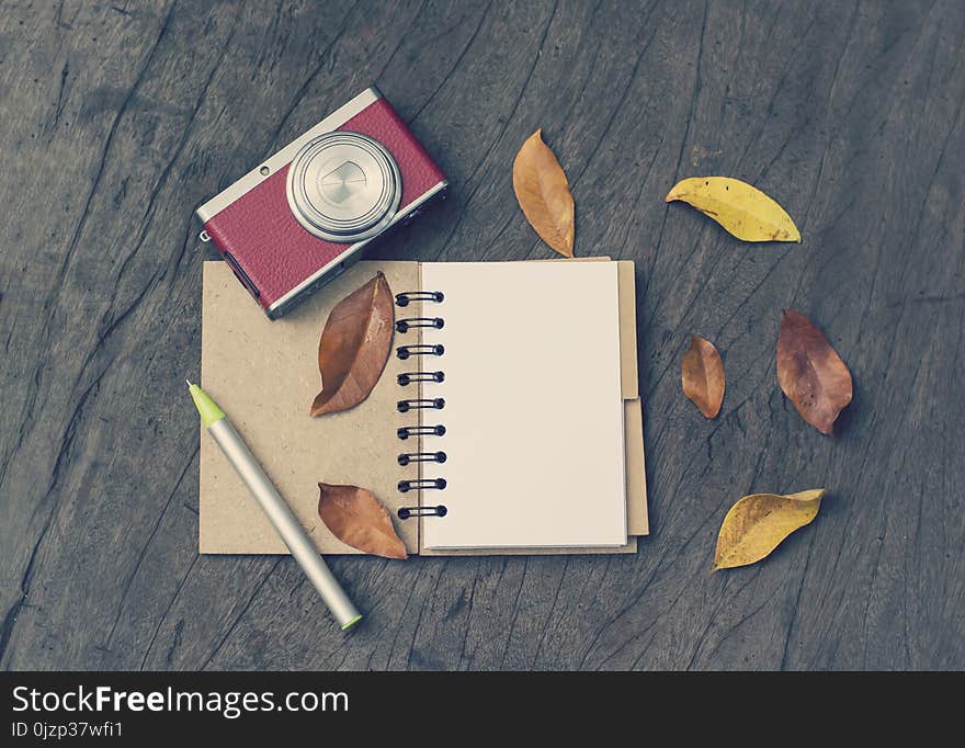 Retro camera, open blank book with dry leaf on wood background