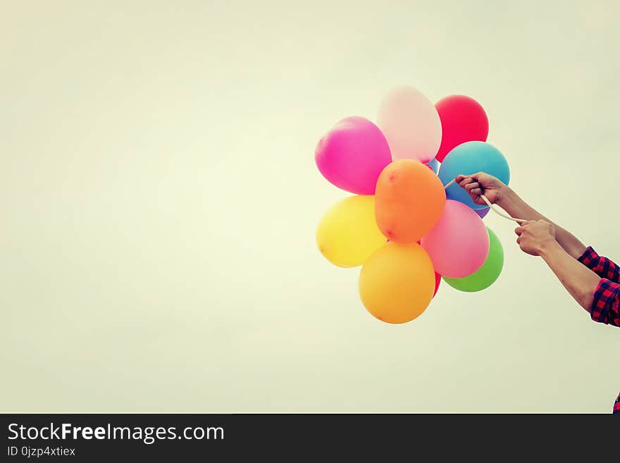 Hand of a teenage girl holding colorful balloons in the sunshine of summer background