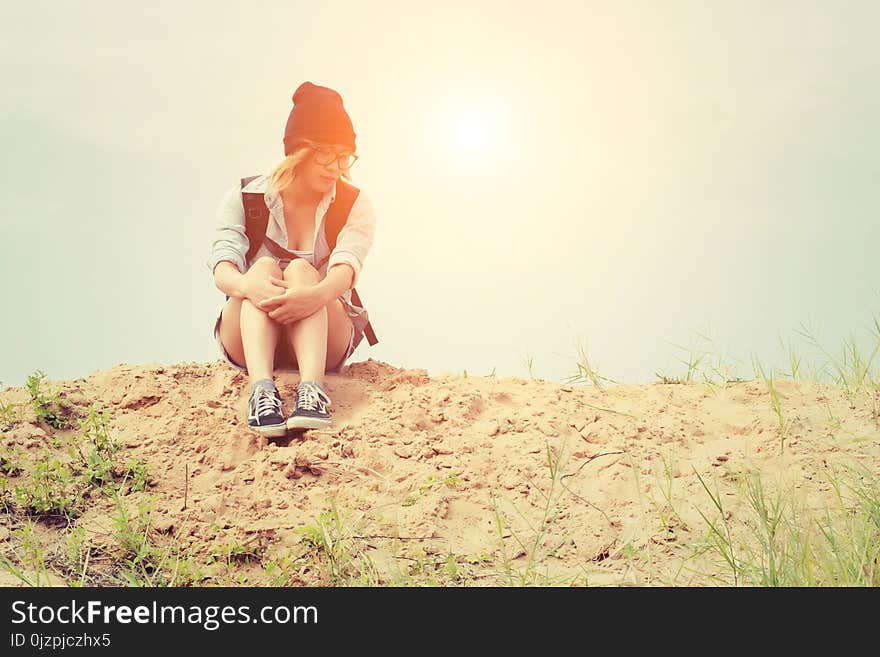 Young hipster woman sitting on the sand and carrying backpack fe