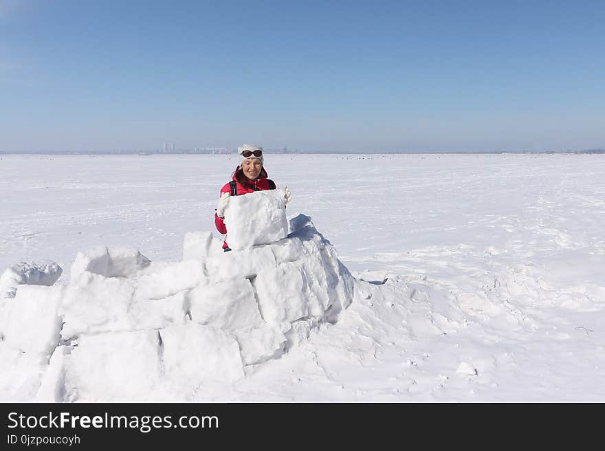 Happy woman a red jacket building an igloo on a snow glade in the winter, Siberia, Russia