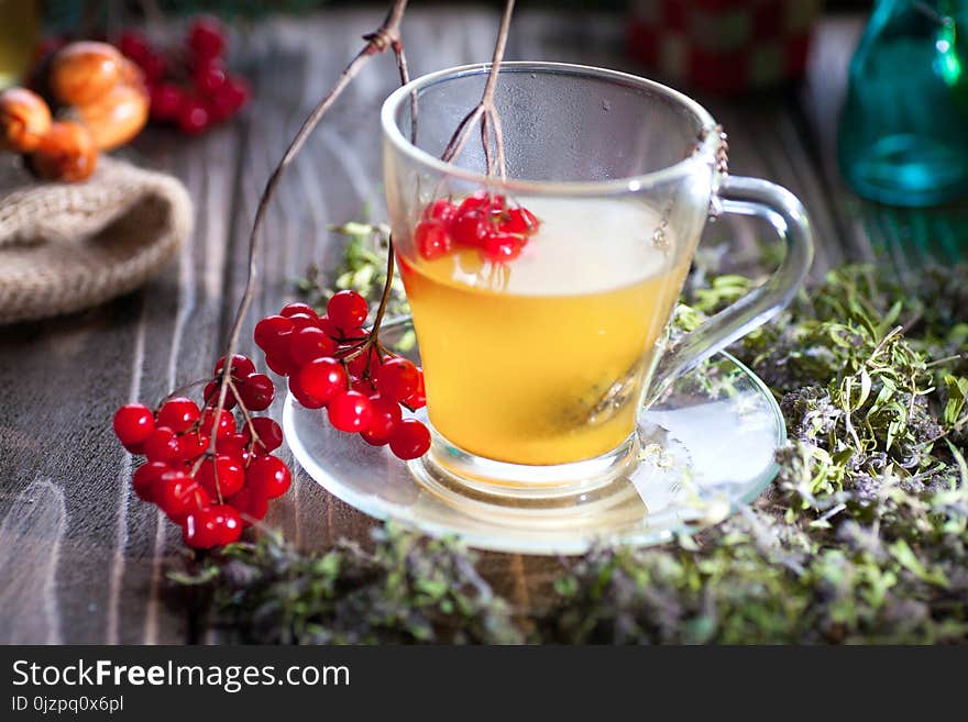 Herbal tea from the viburnum decoction of red sea buckthorn berries and thyme in a transparent glass mug in the village on a wooden table. Herbal tea from the viburnum decoction of red sea buckthorn berries and thyme in a transparent glass mug in the village on a wooden table