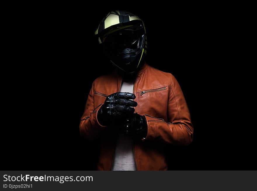 Low Key Male Biker on iSolated Black Background. Complete Biker Suit with Helmet, Wine Color Leather Jacket and Gloves.