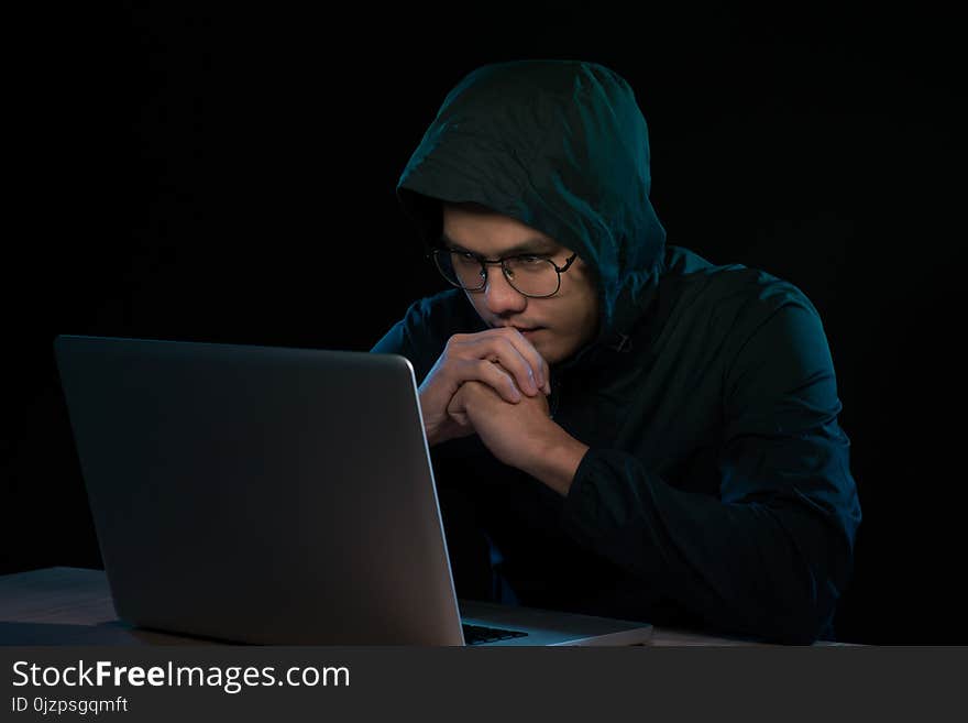 Hacker in a dark hoody sitting in front of a notebook. Computer privacy attack