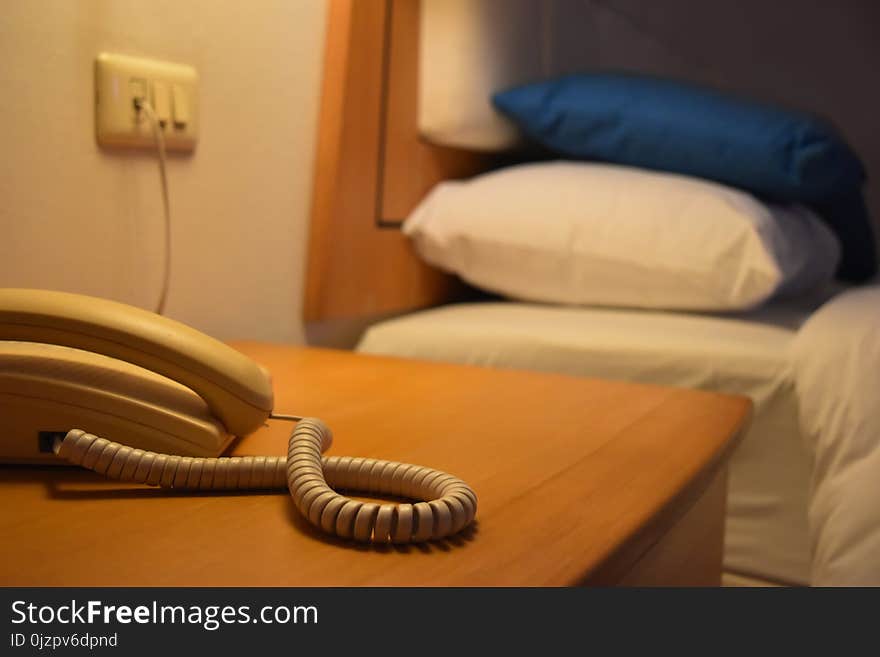 The background in the bedroom is warm color scheme and empty space for text. Telephone is not in use on the wooden table beside the bed and blue and white pillow.