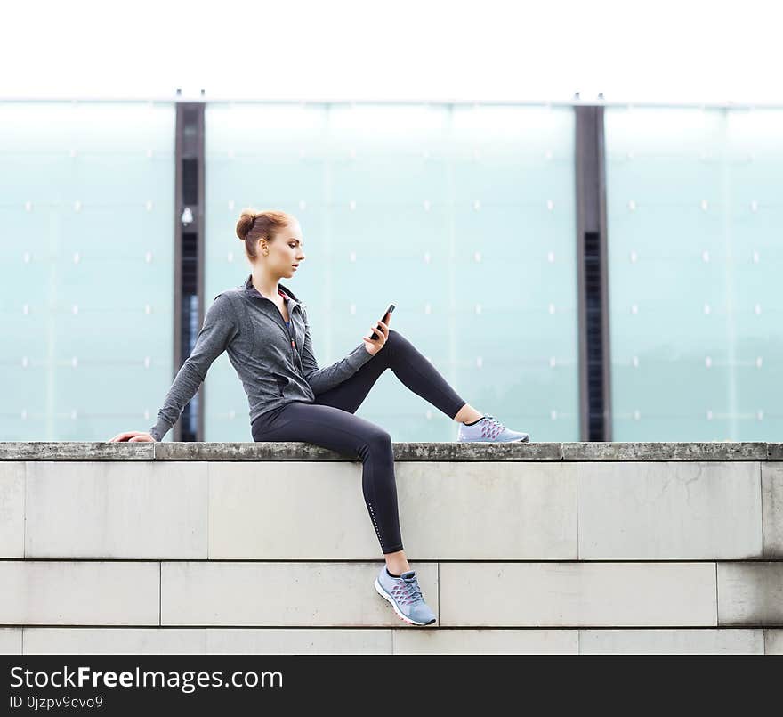 Young, fit and sporty woman sitting on a concrete border. Fitness, sport, urban jogging and healthy lifestyle concept. Young, fit and sporty woman sitting on a concrete border. Fitness, sport, urban jogging and healthy lifestyle concept.