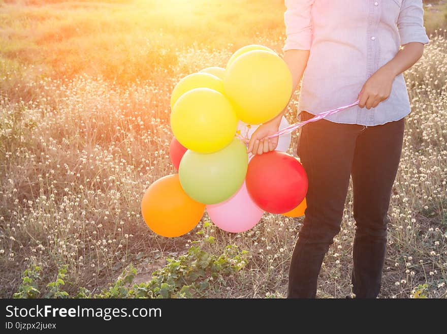 Hipster woman`s hands holding multi color of balloons in the meadows