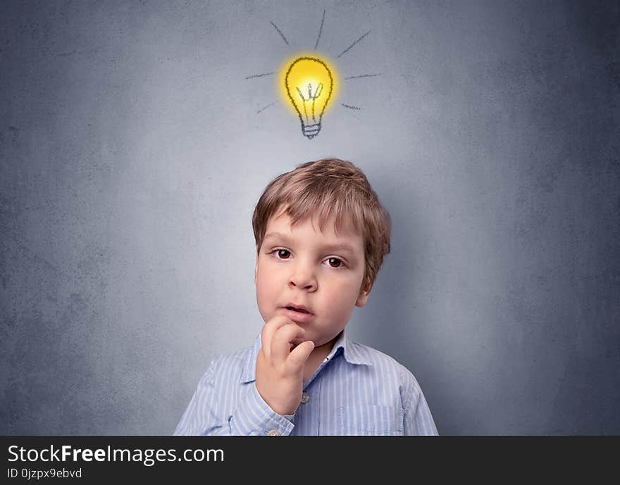 Adorable little kid mull over in front of a grey wall with idea symbol above his head. Adorable little kid mull over in front of a grey wall with idea symbol above his head