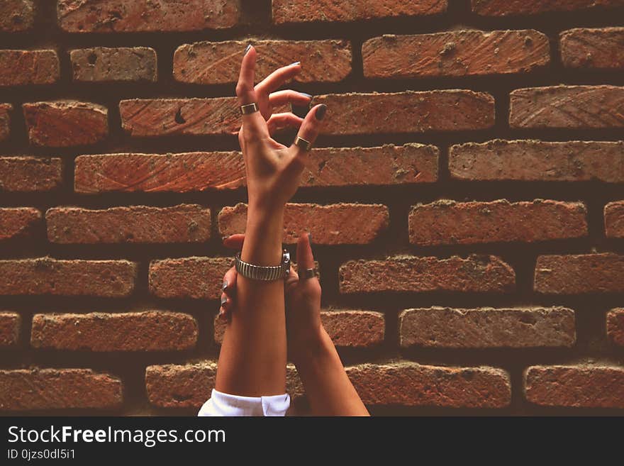 Person Wearing Watch and Rings Raising Left Hand Near Brick Wall