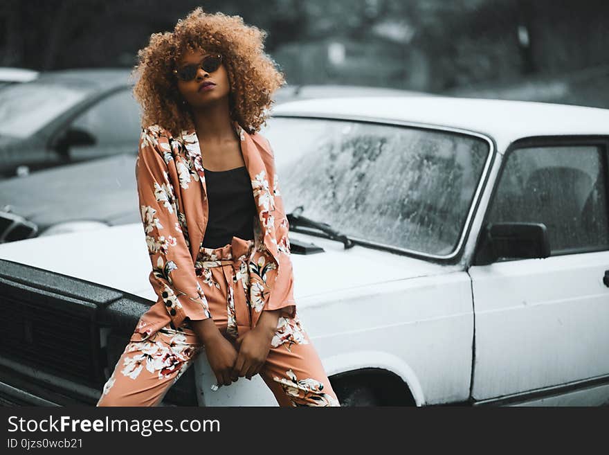 Woman Wearing Brown Floral Print Coat and Pants Sitting on Car