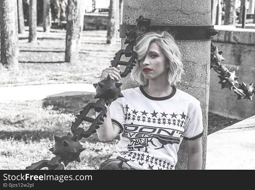 Selective Color Photography of Woman Laying Her Back at Concrete Column Holding Spike Chain