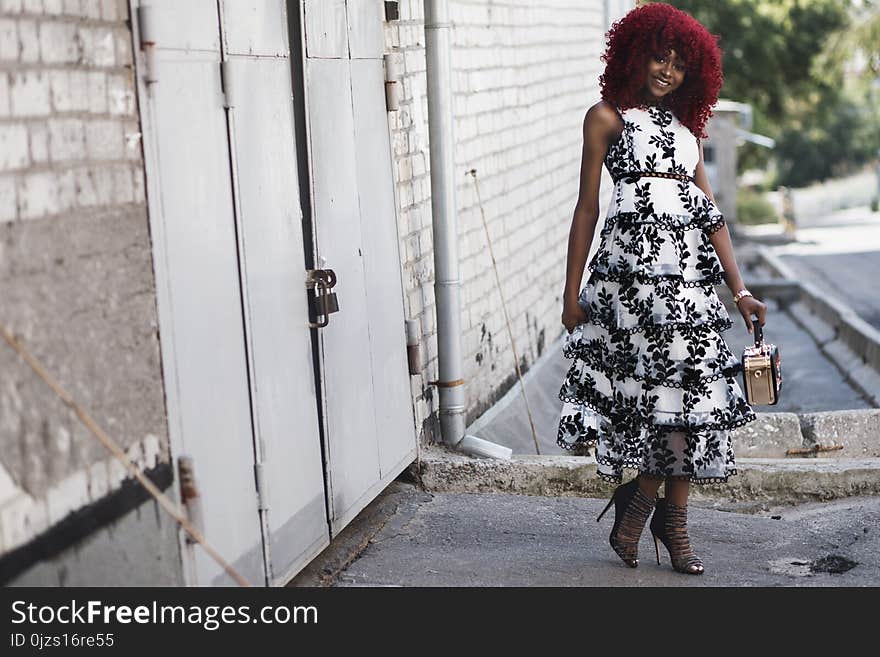 Woman Wearing White and Black Floral Sleeveless Dress Standing Beside White Painted Building