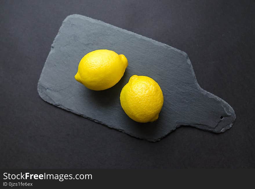 Two Lemons on Black Wooden Pad