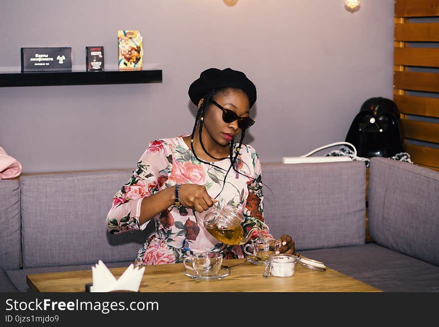 Woman Sitting on Sofa in Front of Table While Holding Clear Glass Teapot