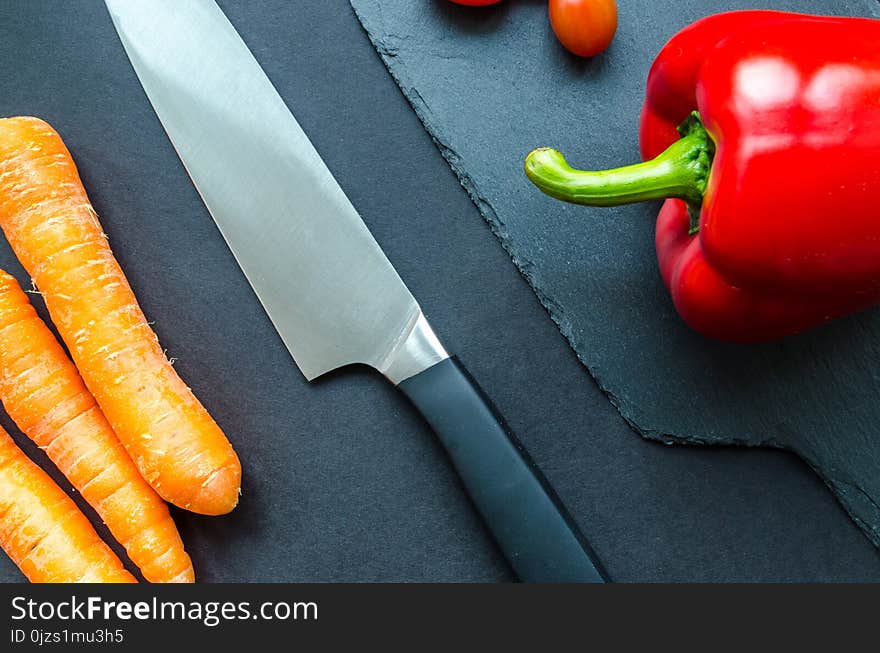 Black Handled Gray Kitchen Knife Beside Orange Carrots and Red Bellpepper