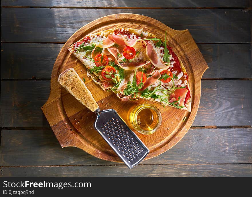 Italian pizza with ham, tomatoes, cheese and herbs on vintage wooden background.