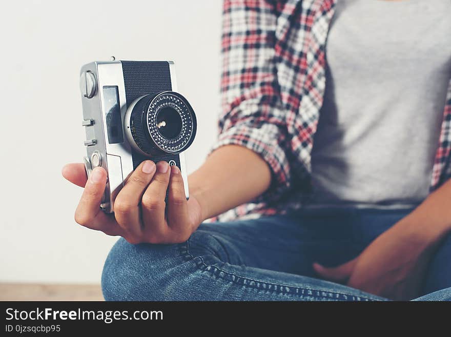 Young hipster photographer hand holding retro camera sitting on wooden floor background