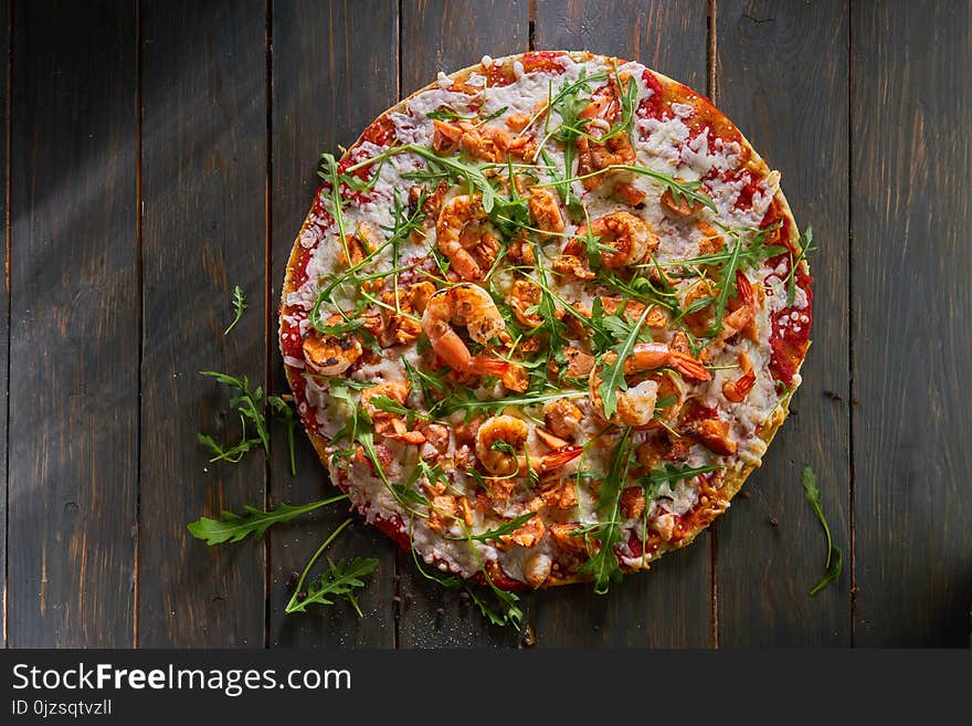 Tasty pizza with shrimp, mozzarella and arugula on a wooden table. Tasty pizza with shrimp, mozzarella and arugula on a wooden table.