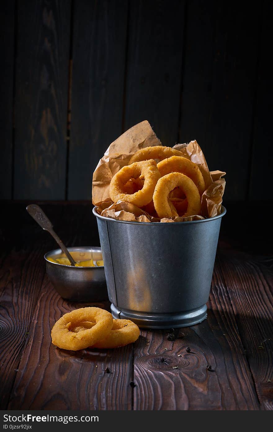 Fried onion rings with sauce served in metal backet on wooden table