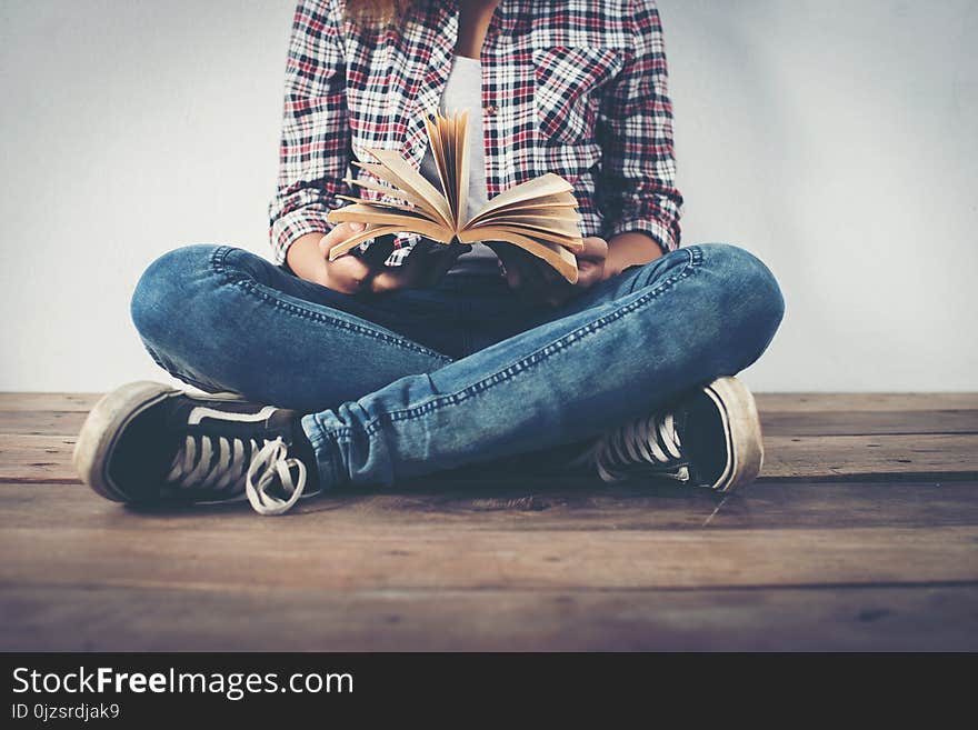 Close-up of hipster woman hands holding open book sitting on wooden floor.