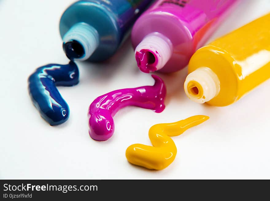 Tubes with acrylic blue, yellow and pink paint on white background