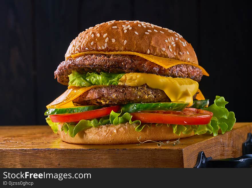 Closeup of home made beef burgers with lettuce and mayonnaise served on little wooden cutting board. Dark background. Closeup of home made beef burgers with lettuce and mayonnaise served on little wooden cutting board. Dark background