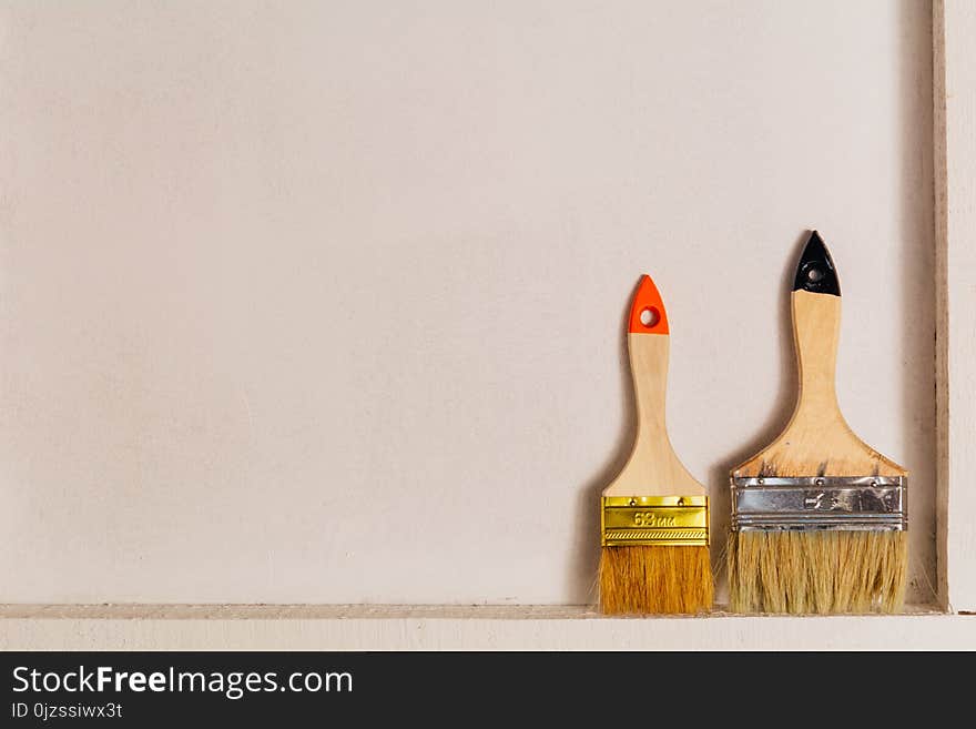 Two paint brushes, standing on the bars and leaning against a white wall