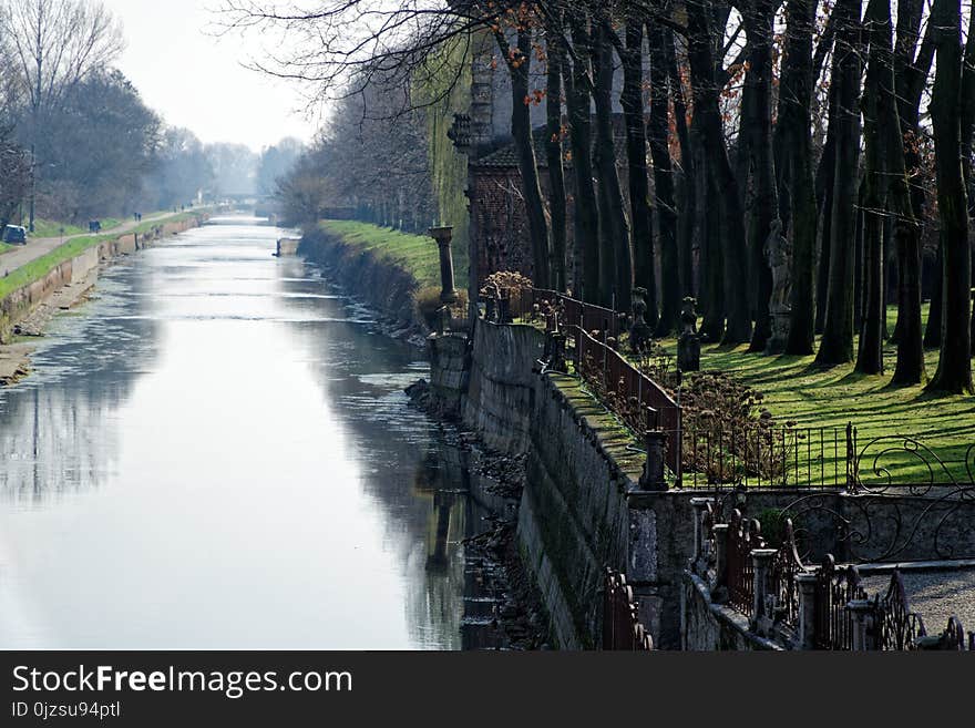 Water canal in spring day, sidewalk along river bank.