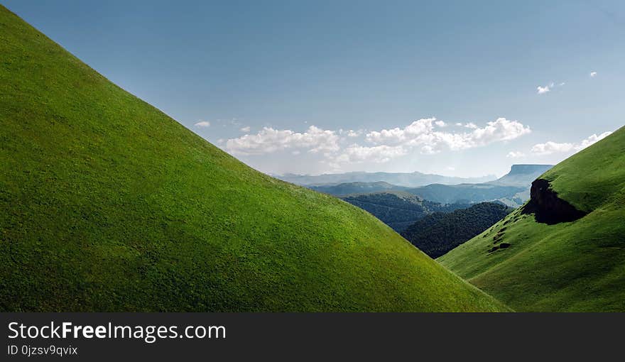 Green hills and mountain range on a sunny day against a background of clouds. Picturesque mountain landscape. Elbrus Region, Northern Caucasus, Russia. Green hills and mountain range on a sunny day against a background of clouds. Picturesque mountain landscape. Elbrus Region, Northern Caucasus, Russia