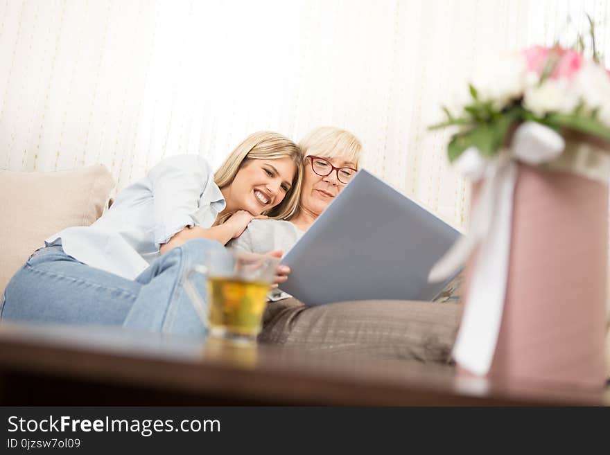 Mother and daughter watch a family photo album, remembering beautiful moments. Mother and daughter watch a family photo album, remembering beautiful moments.