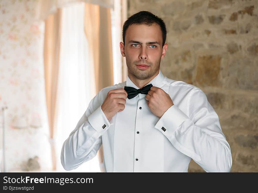 Morning of the groom. Businessman morning preparation. Young and handsome groom getting dressed in a wedding shirt