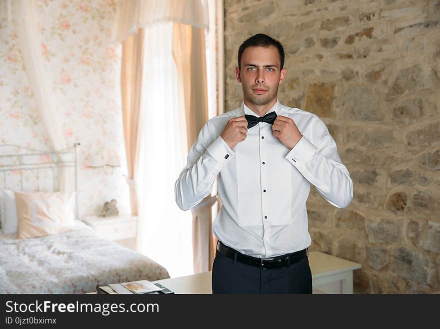 Morning of the groom. Businessman morning preparation. Young and handsome groom getting dressed in a wedding shirt