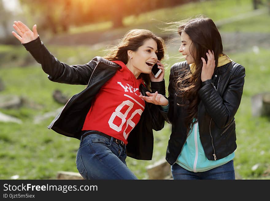 Two Pretty And Happy Young Woman Using The Mobile Phone In The Park. Best Friends.