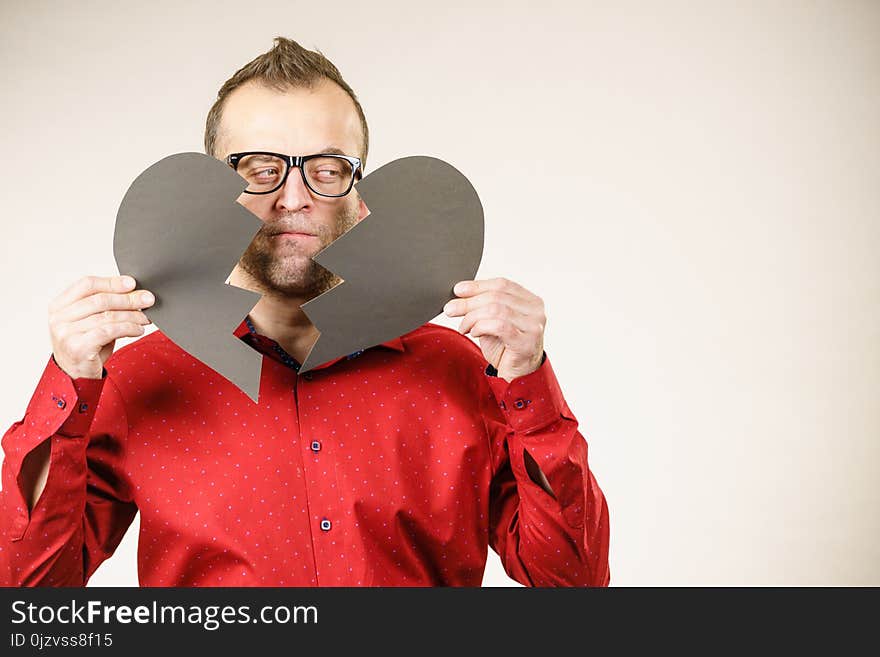 Depression, sadness, relationship problem concept. Man with broken heart full of negative sad emotions. Adult male holding two black halves of love symbol, on grey. Depression, sadness, relationship problem concept. Man with broken heart full of negative sad emotions. Adult male holding two black halves of love symbol, on grey