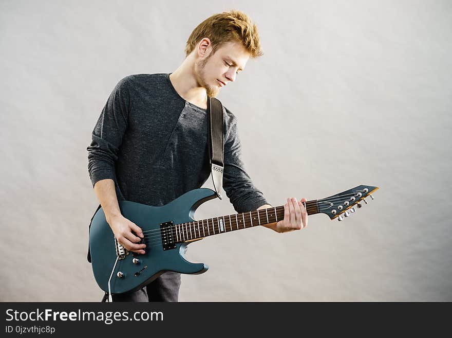 Young bearded man with electric guitar. Adult person is holding instrument and playing. Hobby, music concept, on grey. Young bearded man with electric guitar. Adult person is holding instrument and playing. Hobby, music concept, on grey