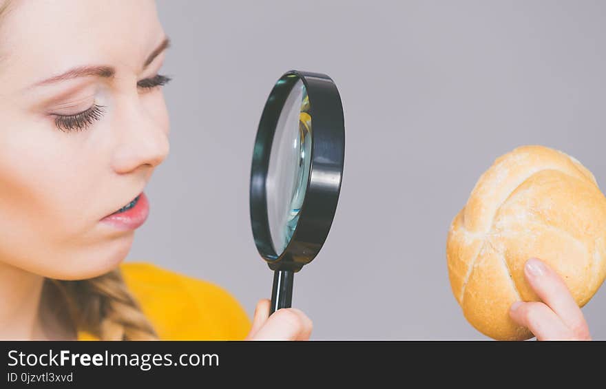 Woman holding bun bread roll and magnifying glass examine wheat product ingredients